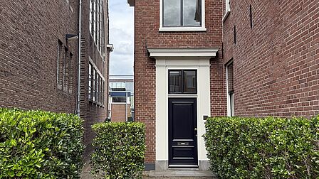 Narrow brick pathway leading to a dark blue front door of a red-brick building